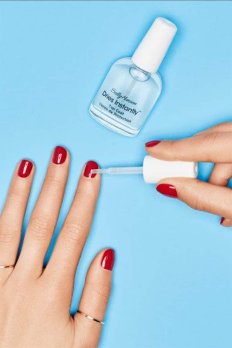 Close up of female hands painting nails with clear nail polish.