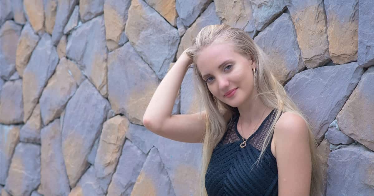 Smiling woman wearing little black dress while leaning against wall outside.