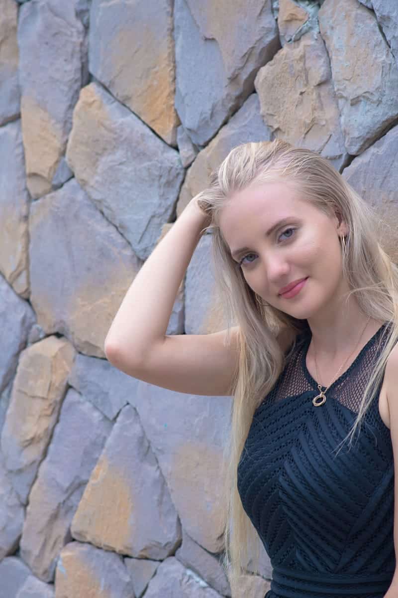 7 Fun & Affordable Little Black Dress Styles 1 Smiling woman wearing little black dress while leaning against wall outside.
