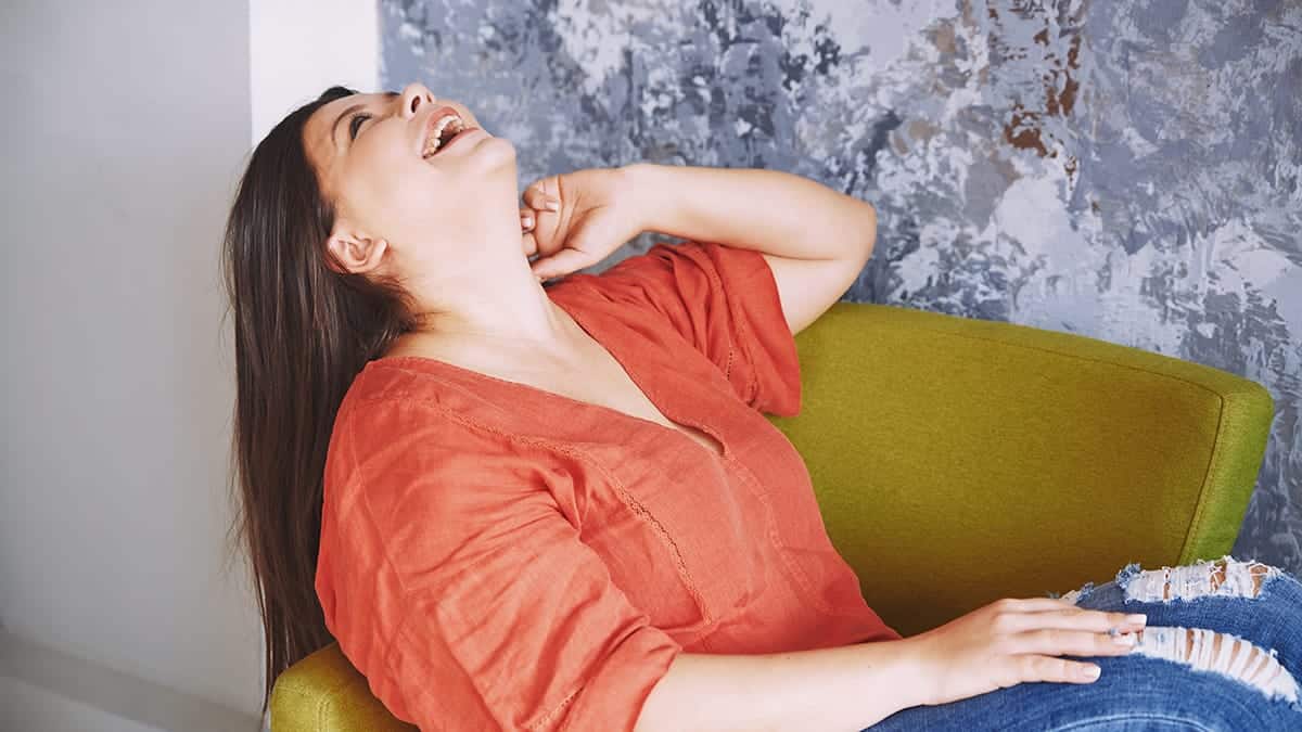 Stylish woman laughs while sitting on chair.