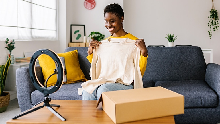Fashion blogger holds up sweater in front of camera to demonstrate how to start a fashion blog.