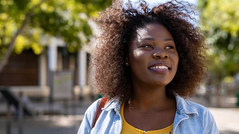 Smiling Black woman with curly hair outside.