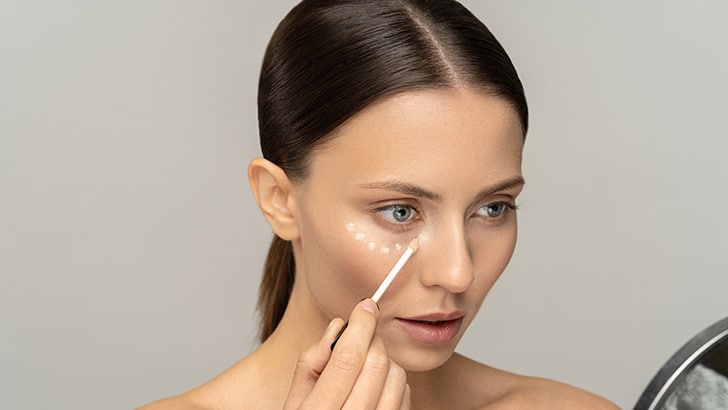 Woman applying concealer under her eye.