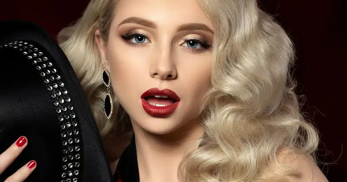 Blond woman with retro makeup and finger waves in her hair holds hat.