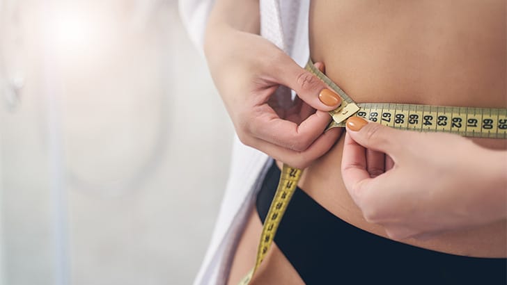 Woman measures natural waist with cloth tape.