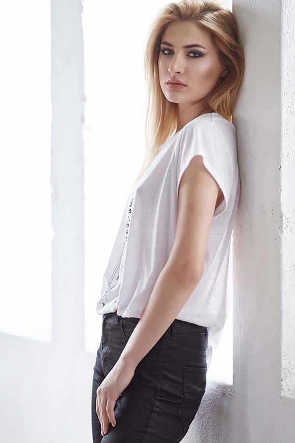 Model wearing white t-shirt leans against wall.