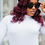 Plus size fashion model wears sunglasses and hat outside.