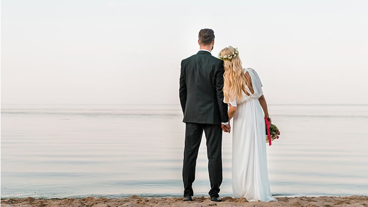 View from behind of bride and groom standing on the beach.