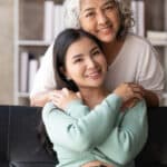 Mother and adult daughter hug and smile.