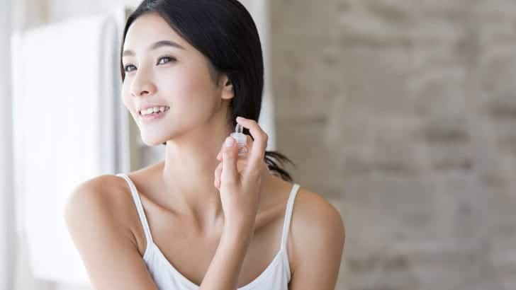 Woman smiles while spraying perfume on her neck.