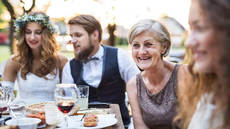 Senior smiling while sitting near bride and groom at wedding.