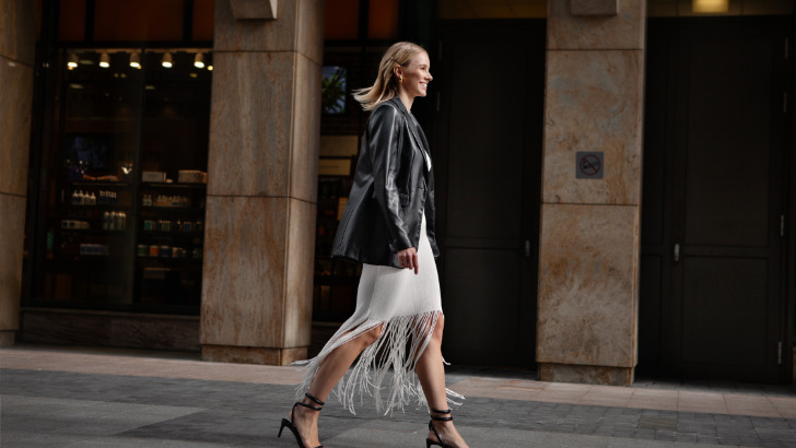 Woman wearing leather blazer walks down street.
