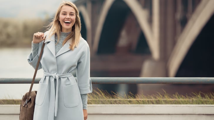 Woman wears trench coat and sweater dress outfit.