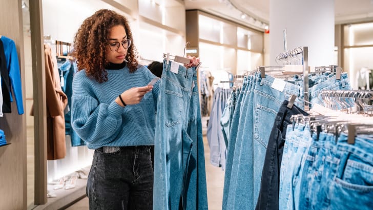 Woman checks price tag of jeans to represent cost per wear concept.