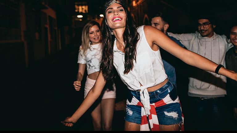 Woman wearing red, white, and blue sweatshirt around her waist, dancing at party.