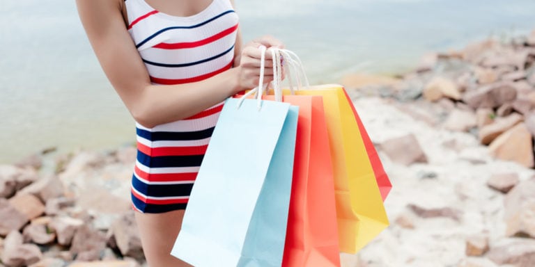Tall woman wearing swimsuit on beach holding shopping bags