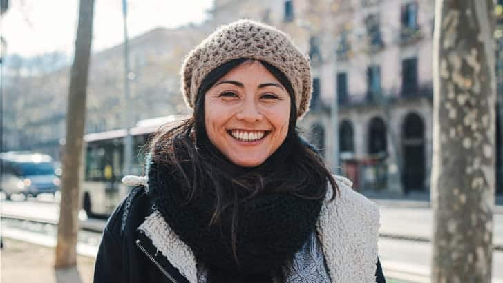 Smiling woman wearing beanie and sweater to demonstrate what to wear while traveling.