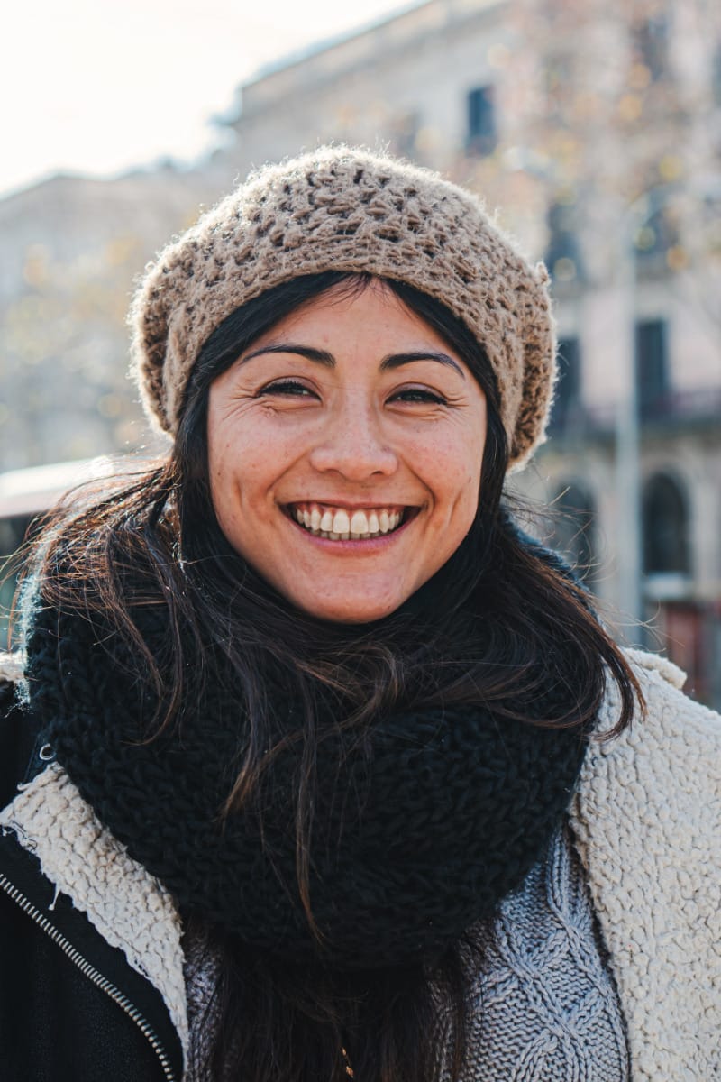 Smiling woman wearing beanie and sweater to demonstrate what to wear while traveling.