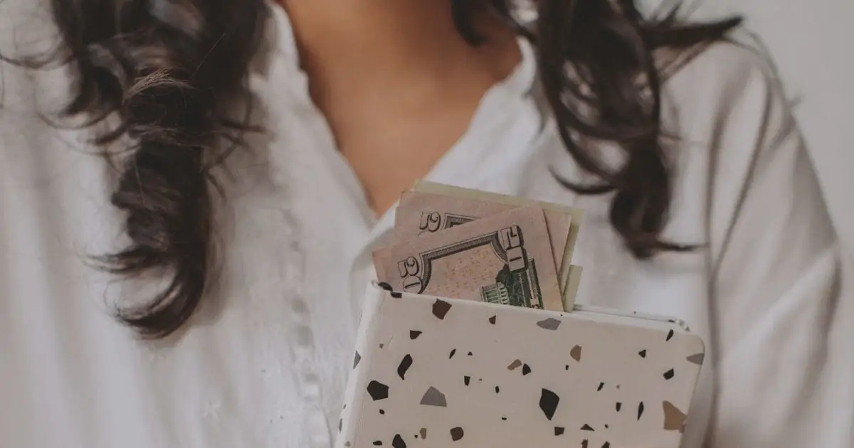 Close-up of woman holding folder with cash sticking out of it.