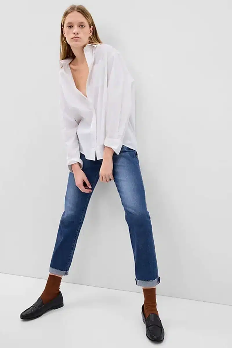 Model wears white button-down top and medium wash denim capri pants.