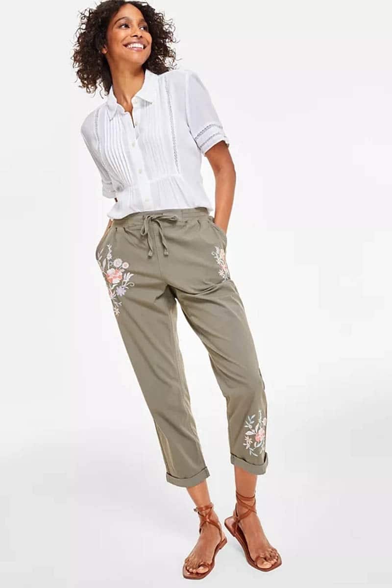 Model wears capri pants with embroidered flower detail. 