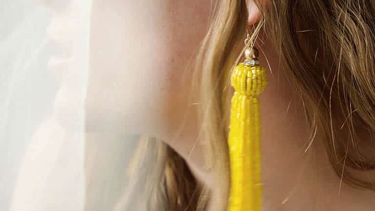 Close-up of woman wearing trendy summer jewelry -- long yellow earrings.