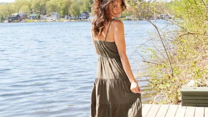 Woman standing at lakefront wearing summer dress turns back to camera.