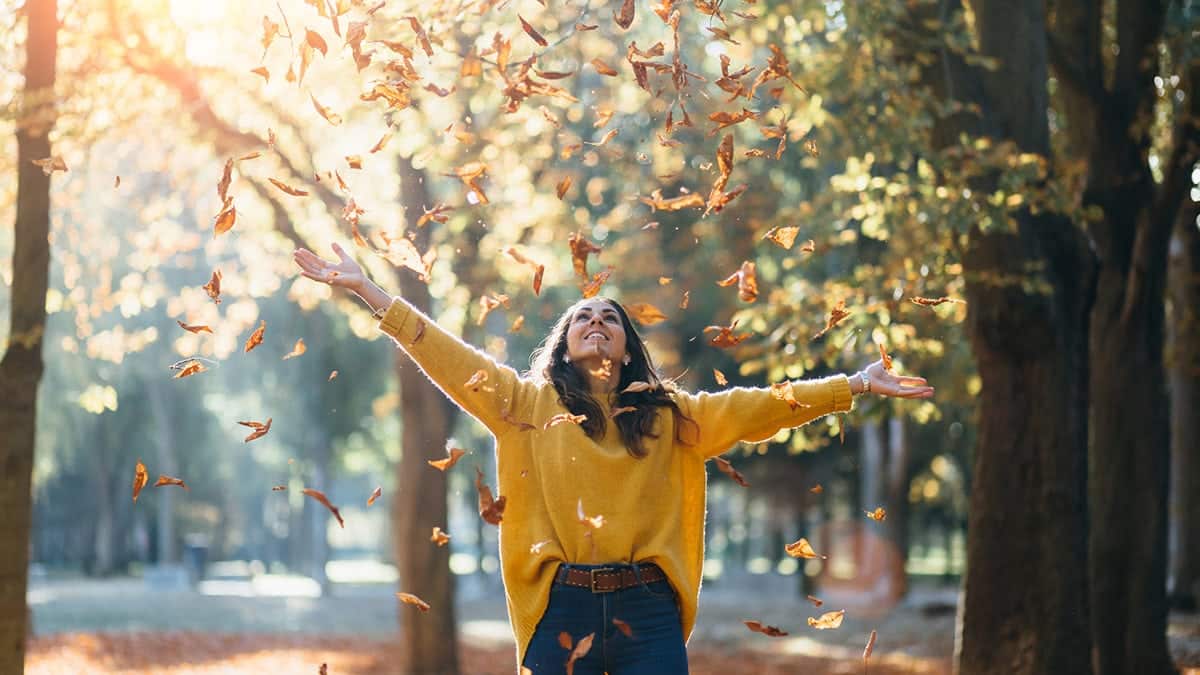 Woman wearing long-sleeve top, throwing fall leaves