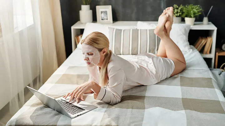 Woman wearing robe at home, on bed with laptop.