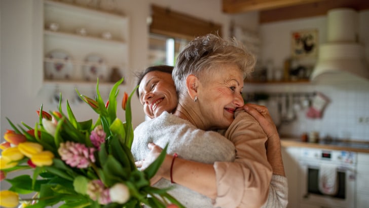 Senior mom hugs adult daughter after receiving Mother's day jewelry gifts.