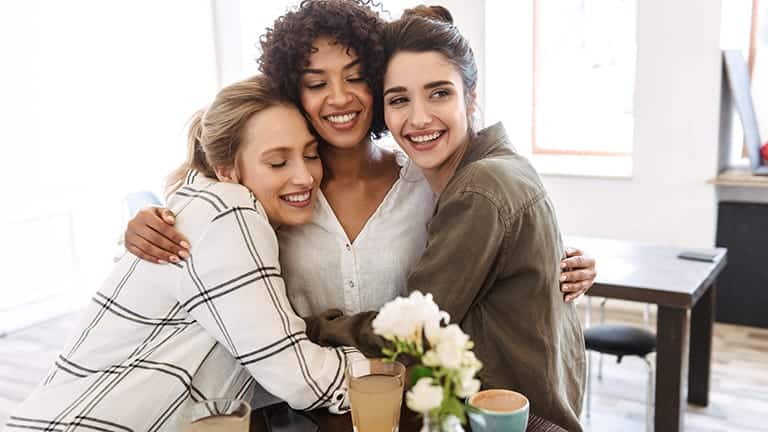 Three young women friends reconnecting over coffee.