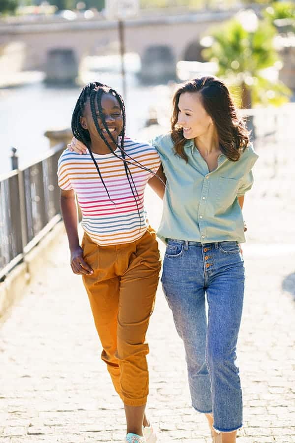 Two young women friends walking down the street together laughing.
