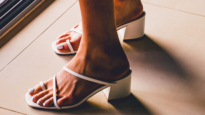 Close up of strappy white heeled sandals on woman's feet.