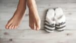 Close up of feet with slippers on the ground in the background.