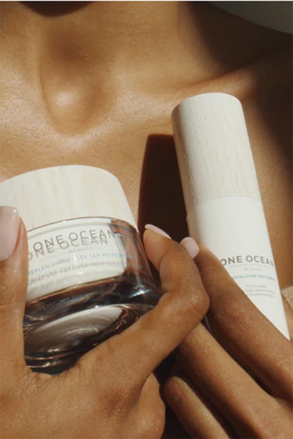 Close up of woman's hands holding two Ocean One beauty products against her chest.