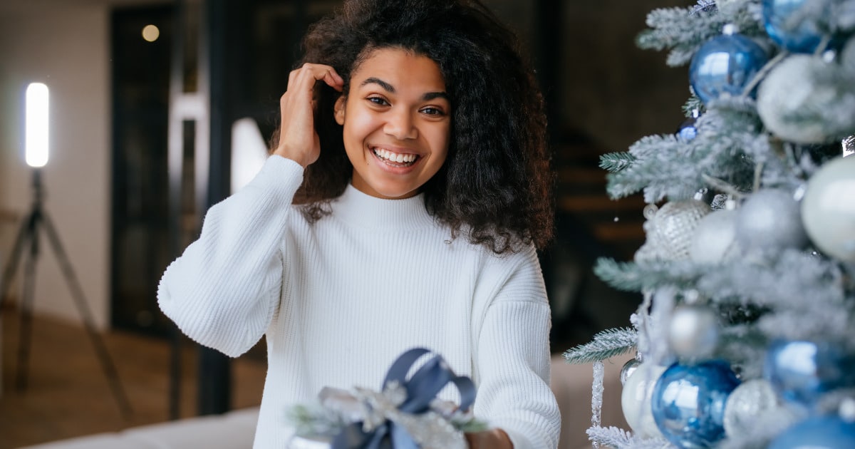 Woman holds holiday gift while smiling.