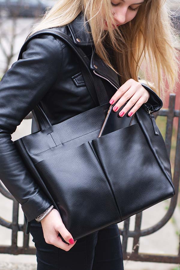 Close-up of woman sliding pen into front pocket of leather bag.