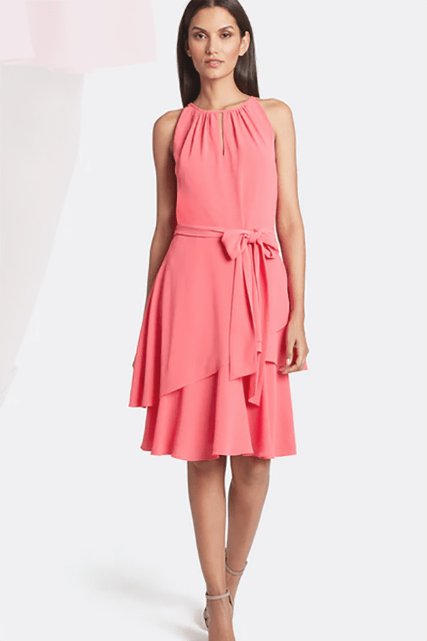 Model wears coral dress with belted waist and tiered skirt.