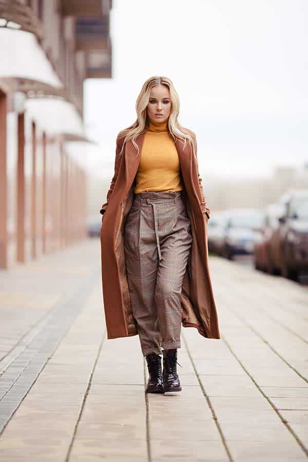 Woman wearing trenchcoat walks on boardwalk outside.