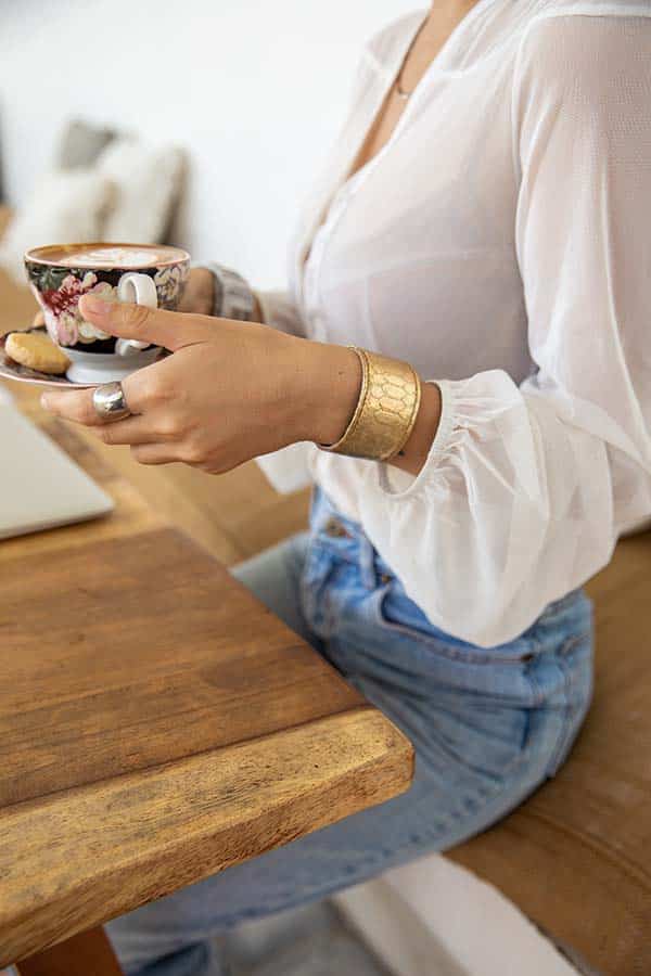 Close-up of woman wearing gold cuff bracelet and white blouse and jeans.