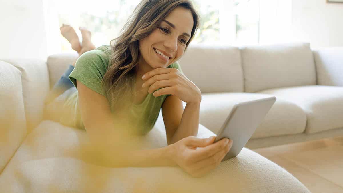 Smiling woman reads email from Shop It To Me while lying on couch at home.