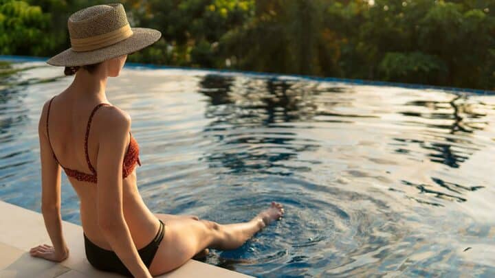 Woman wearing swimwear sits at the end of a pool.