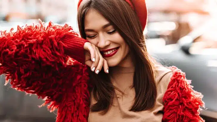 Woman smiles with eyes closed while wearing red lipstick, one of the season's hottest lip colors.