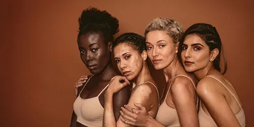 Diverse group of women stand together against brown background.