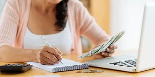 Close-up of woman counting money and writing notes.