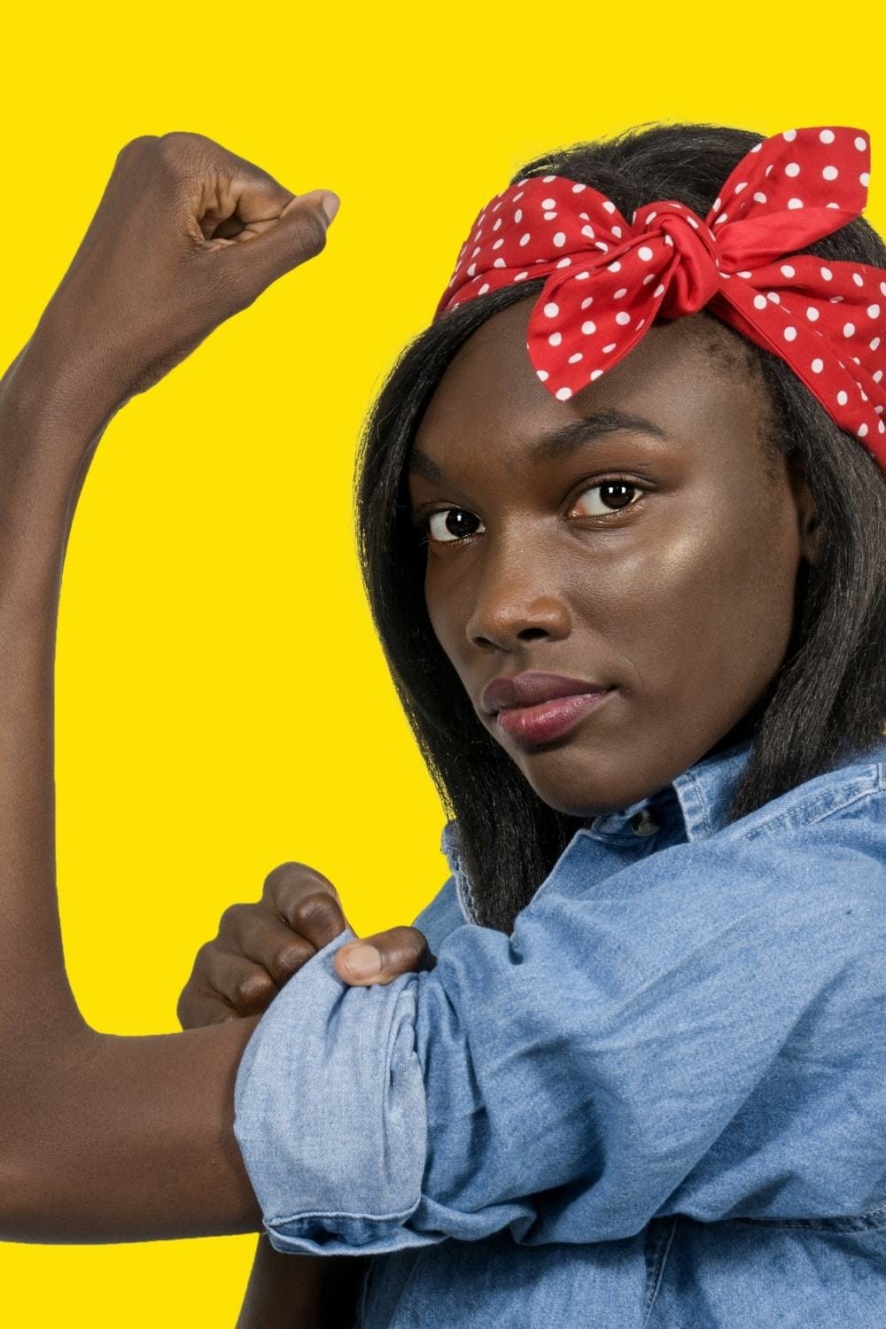 Woman flexes her bicep while wearing a denim shirt and red bandana.