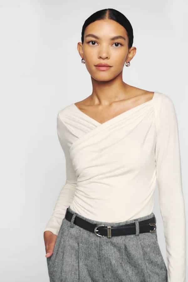 Model wears cream colored long-sleeved top from Reformation.