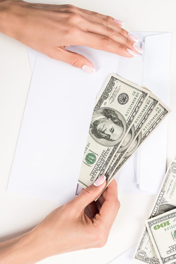 Vue de dessus des mains féminines mettant de l'argent dans une enveloppe.
