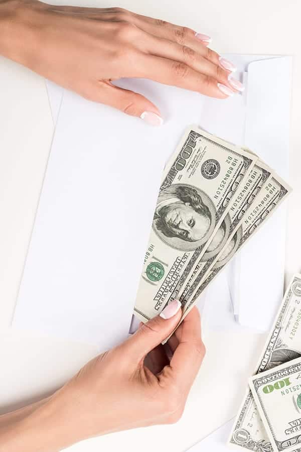 Top view of female hands putting cash into an envelope.