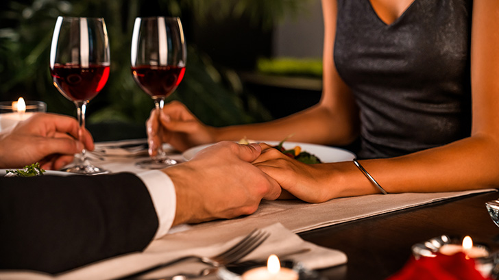 Close up of couple at dinner table, holding hands and wearing date night clothes.